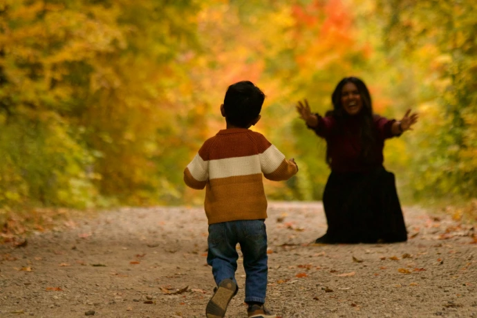 Child running towards a woman in autumn forest